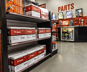 Interior warehouse shelving unit stocked with red and white Toyota forklift parts boxes and components with orange signage overhead