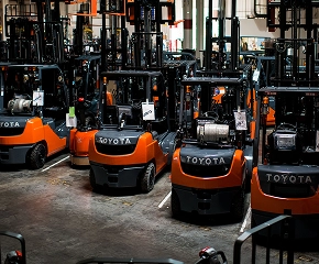 Multiple orange and black Toyota forklifts parked in an outdoor industrial yard with warehouse buildings in background