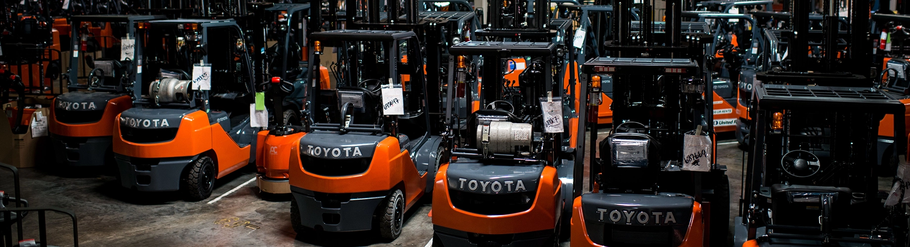 Large indoor warehouse with rows of orange and black Toyota forklifts in various stages of assembly and parts storage on shelving